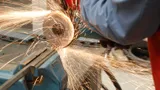 Angle grinder with a cut-off disc slicing through a steel bar clamped in a vise, throwing sparks