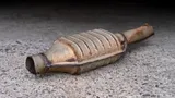 Used catalytic converter with exhaust pipe stubs, lying on pavement