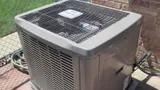 Central air conditioner condenser unit on a pad beside a brick house