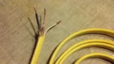 Yellow NM-B (Romex) cable with the outer jacket stripped back to show black, white, and bare copper conductors