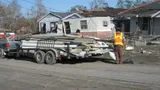 Worker beside a trailer loaded with salvaged metal siding outside a damaged house