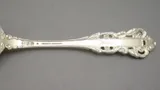 Back of an ornate sterling silver spoon handle stamped with the maker’s marks and the word STERLING
