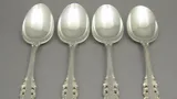 Four ornate sterling silver spoons laid side by side on a grey background